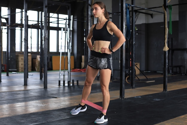 Muscular and strong girl doing exercises use fitness rubber at gym.