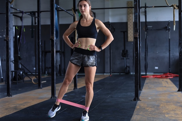 Muscular and strong girl doing exercises use fitness rubber at gym.