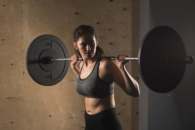 Muscular woman in a gym doing heavy weight exercises with barbell