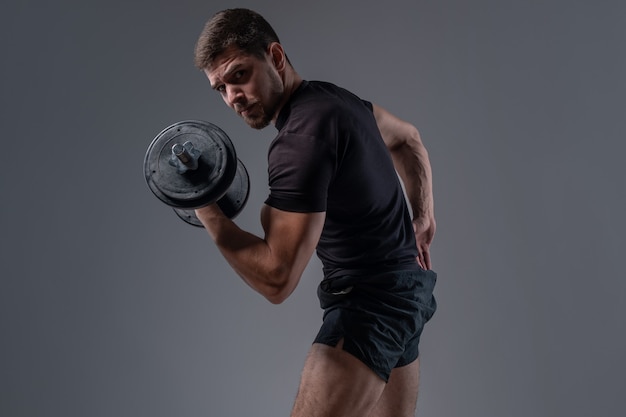 Muscular young bodybuilder doing bicep curl with dumbbell