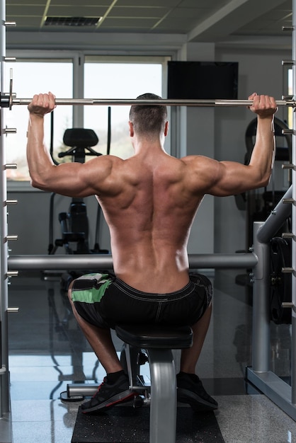 Muscular Young Man Doing Heavy Weight Exercise For Shoulders In Gym