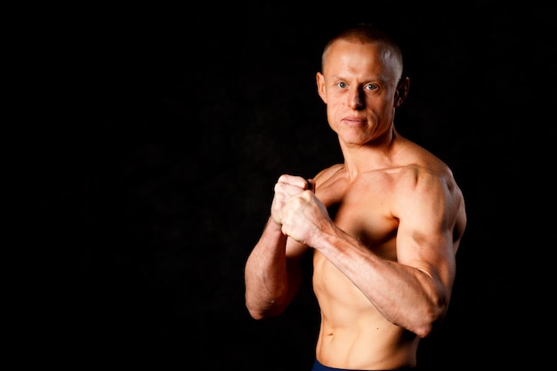 Muscular young man in studio on dark background shows the different movements and body parts