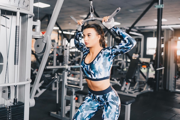 Muscular young woman doing exercises on the simulator in the gym. Fitness, workout bodybuilding health care concept.