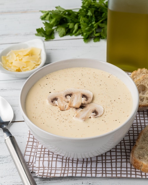 Mushroom soup in a bowl with bread slices and seasonings over wooden table