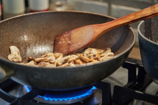 Mushrooms are fried in pan on gas stove in the kitchen.