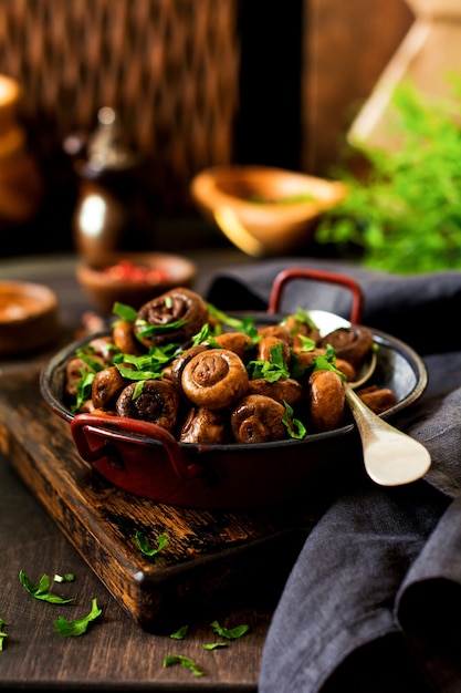 Mushrooms champignon fried in soy sauce, with pepper and steamed onions in an old metal bowl on an old vintage table. Selective focus