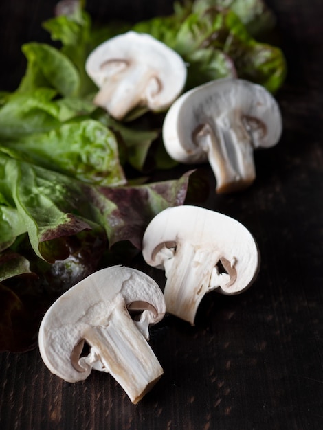 Mushrooms champignons fresh in cut form surrounded by greenery on a dark wooden background