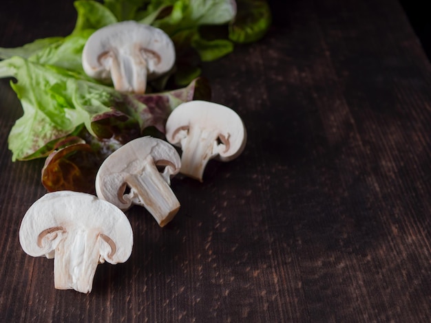 Mushrooms champignons fresh in cut form surrounded by greenery on a dark wooden background