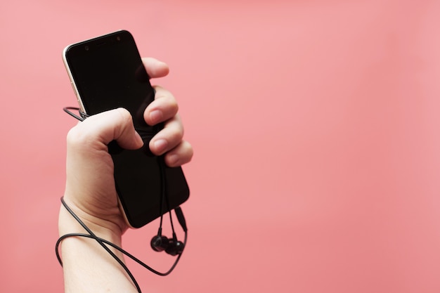 Music addiction concept, smartphone tied to hand with wire on pink background. High quality photo