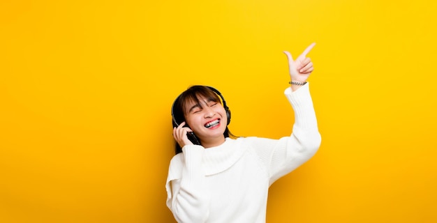 Music listening to music Beautiful Asian woman in headphones listening to music and enjoying the sound of music on a yellow background