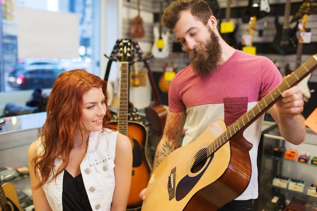 music, sale, people, musical instruments and entertainment concept - happy couple of musicians with guitar at music store