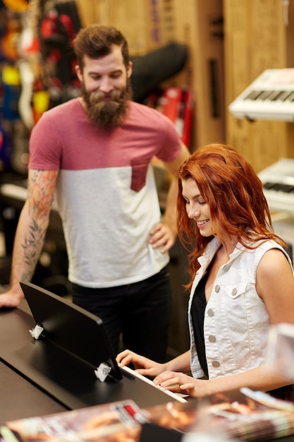 music, sale, people, musical instruments and entertainment concept - happy man and woman playing piano at music store