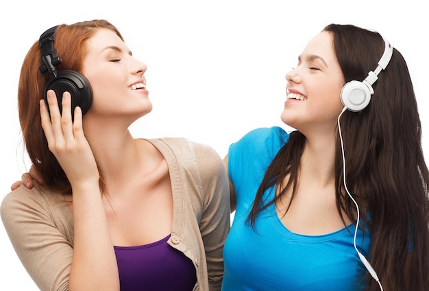 music and technology concept - two smiling teenagers with closed eyes listeting to music with headphones