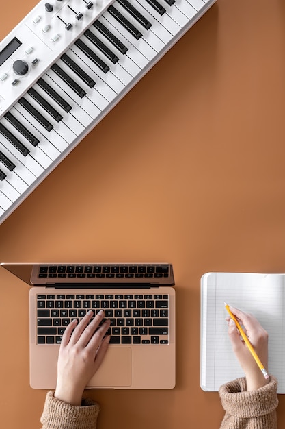 Musical background with musical keys, laptop and female hands, top view.