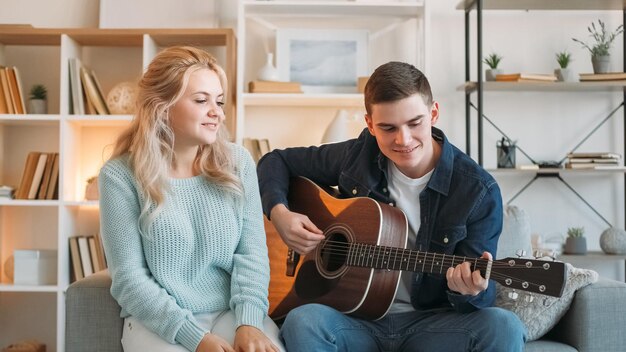 Musical date romantic hobby happy man playing acoustic guitar for cheerful woman family enjoying