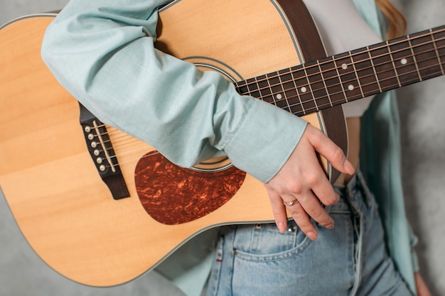 Musical instrument acoustic guitar in the hand of a woman dressed in a blue shirt and jeans