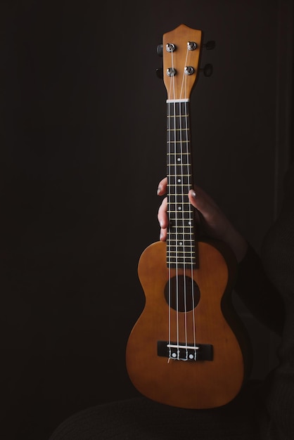 Musical instrument ukulele in a woman's hand on a dark background