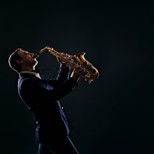 Photo musician plays jazz at saxophone. dark