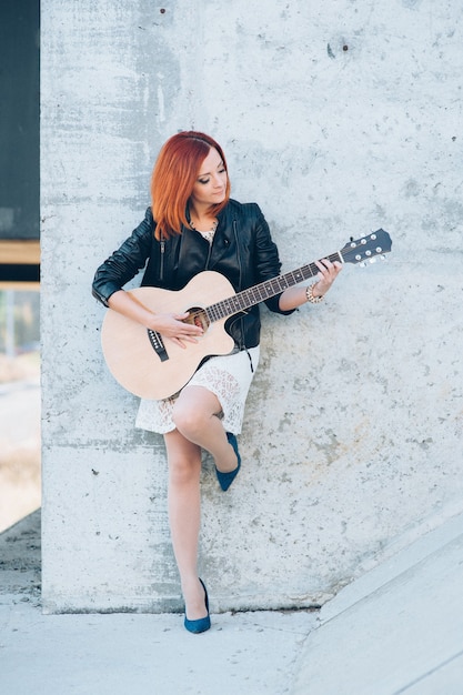 Musician young woman with red hair with an acoustic guitar