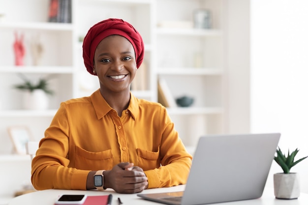 Muslim african american woman posing at office working on laptop