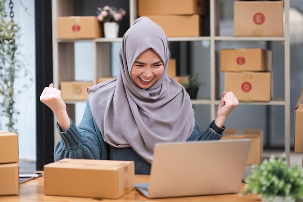 Muslim asian woman freelancer entrepreneur Smile for sales success after checking order from online shopping store in a laptop at home office Concept of merchant business online and eCommerce