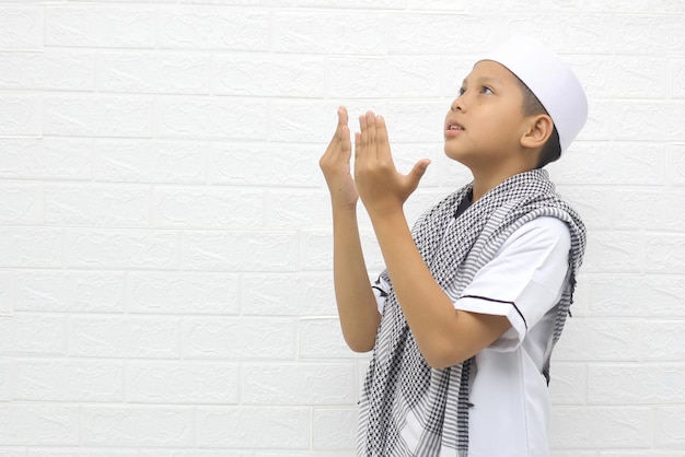 Muslim boy raising both hands in a gesture of praying asking Allah on a white background with copy