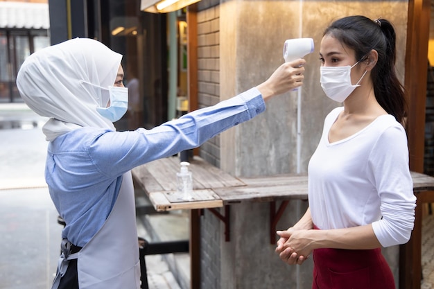 Muslim business staff or shop keeper checking fever of customer by thermo scan device