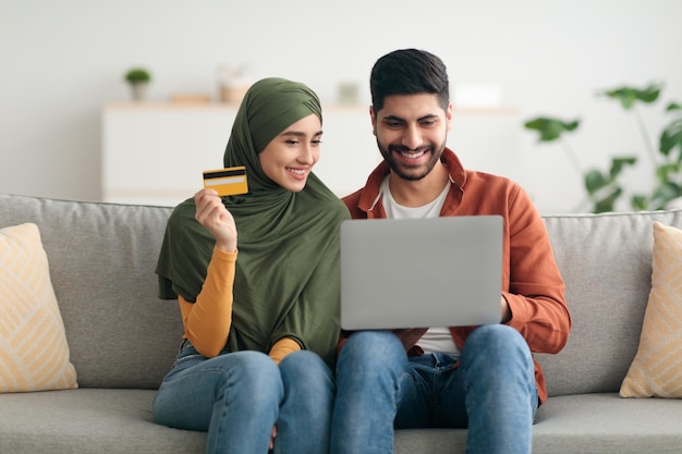 Muslim couple shopping online via laptop and credit card indoors