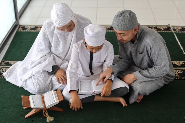 muslim family parents with children reading Quran and praying together at the mosque