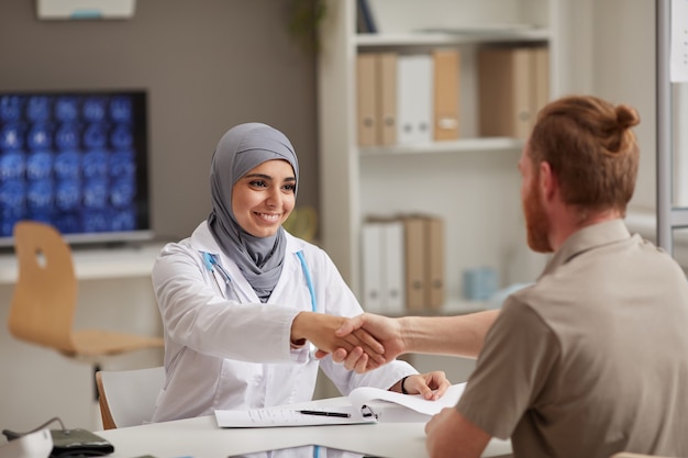 Muslim female doctor shaking hand with her patient during meeting at hospital