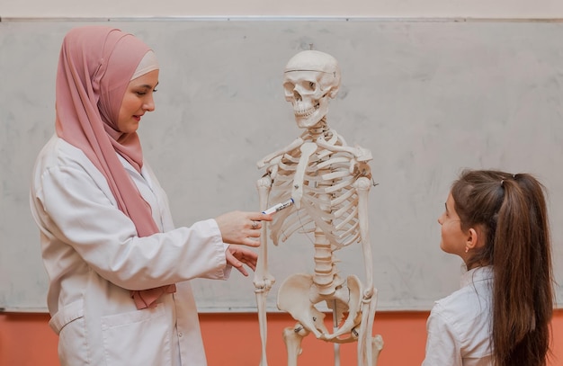 A Muslim female teacher using the human body skeleton model to explain anatomy in the classroom lab