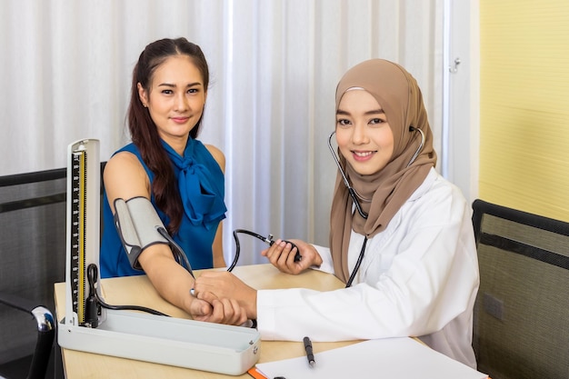 Muslim female woman medical doctor examining and measure blood pressure patient sitting on chair looking at camera