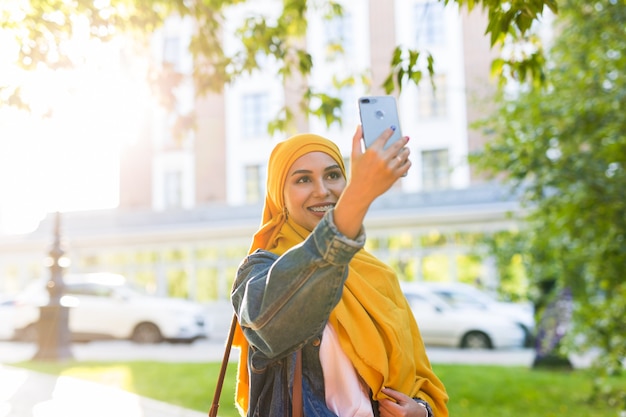 Muslim girl in hijab makes a selfie on the phone standing on the street of the city