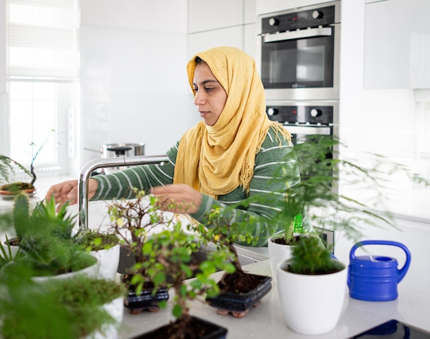 Muslim housewife at home watering plants in kitchen