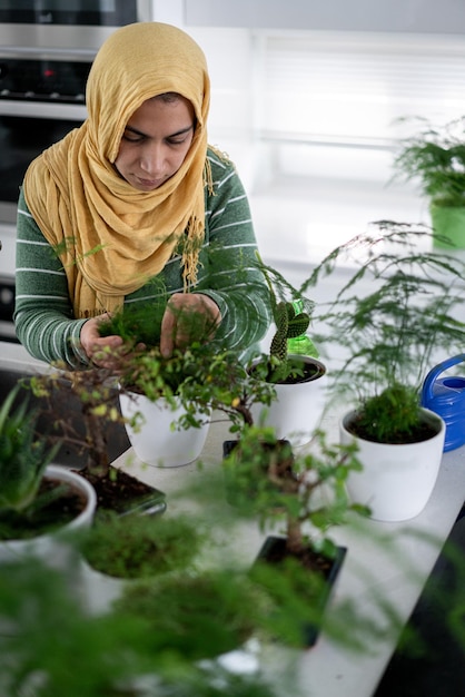 Muslim housewife at home watering plants in kitchen