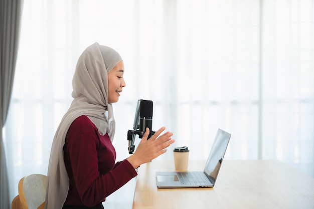 Muslim Islam freelance entrepreneur woman wearing hijab and talking while conference meeting working using microphone and laptop and on desk table at the home office Business conference technology