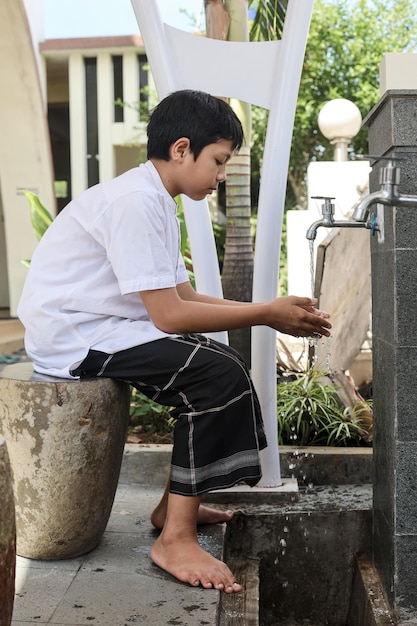 Muslim kid washing hands using water outside the mosque, procedure of ablution before praying salah