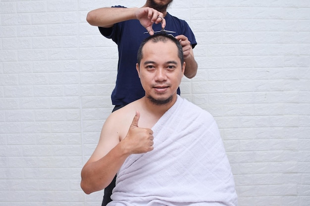 Muslim man wearing white ihram clothes doing Tahallul, shaving their head after performing tawaf and