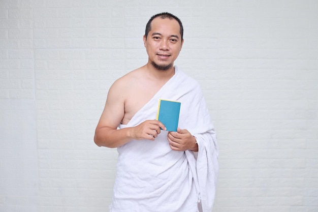 Muslim man wearing white ihram clothes and holding passport ready for Hajj or umrah, standing over w