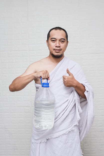 Muslim man wearing white ihram clothes and showing a bottle of zam zam water