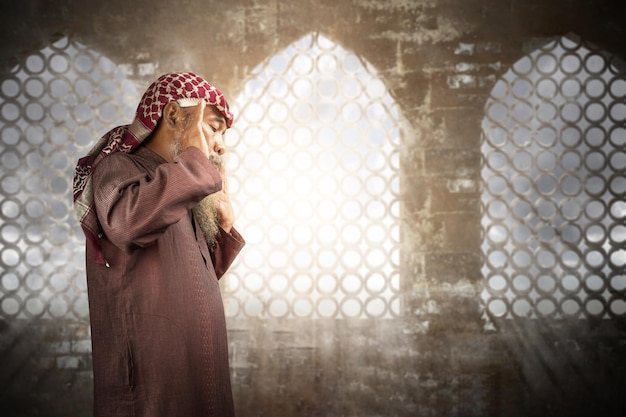 Muslim man with a beard wearing keffiyeh with agal in praying position salat on the prayer rug