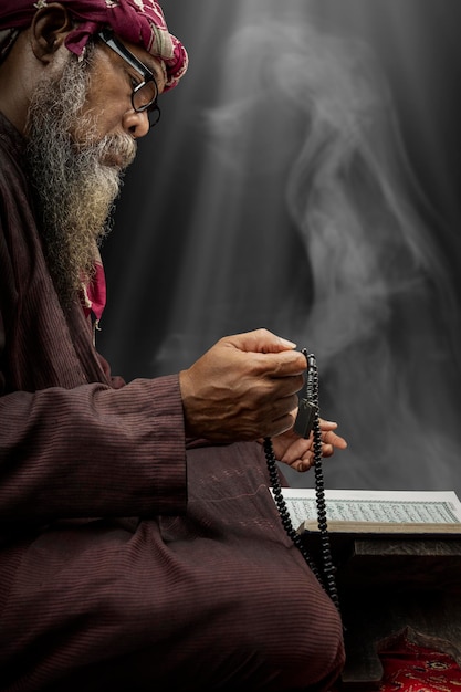 Muslim man with a beard wearing keffiyeh with agal praying with prayer beads on his hands