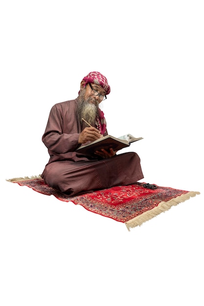 Muslim man with a beard wearing keffiyeh with agal sitting and reading the Quran on the prayer rug