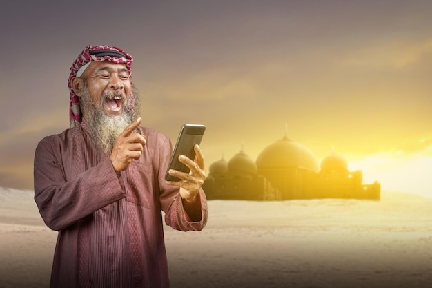 Muslim man with a beard wearing keffiyeh with agal using mobile phone