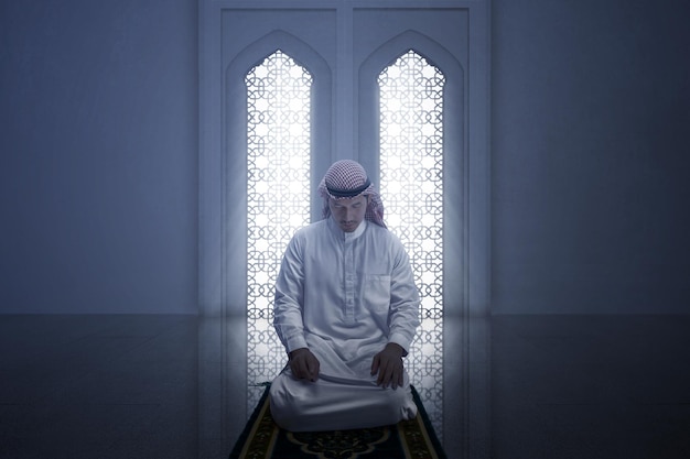 Muslim man with keffiyeh with agal in praying position salat on the prayer rug