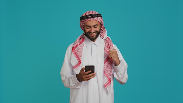 Muslim person in traditional costume having smartphone in hands and typing in internet social media messaging Young adult browsing on mobile phone and texting internet webpage