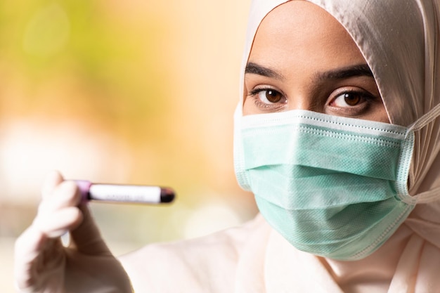 Muslim Woman Doctor With Surgical Mask and Gloves Holding a Blood Test Tube Which is Signed as Covid-19