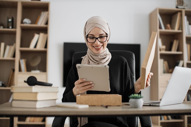 Muslim woman doing live stream while unpacking box with new tablet