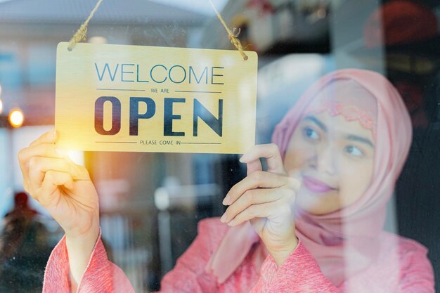 Muslim woman hand of staff woman turning open sign board on glass door in modern cafe coffee shop hotel service cafe restaurant retail store small business owner food