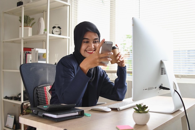 Muslim woman using smartphone in office. Entrepreneur businessman, freelancer, sits at her office de